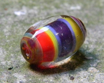 Multicoloured Clown is a deeply encased oval focal bead created with raku, purple, red and yellow glass.