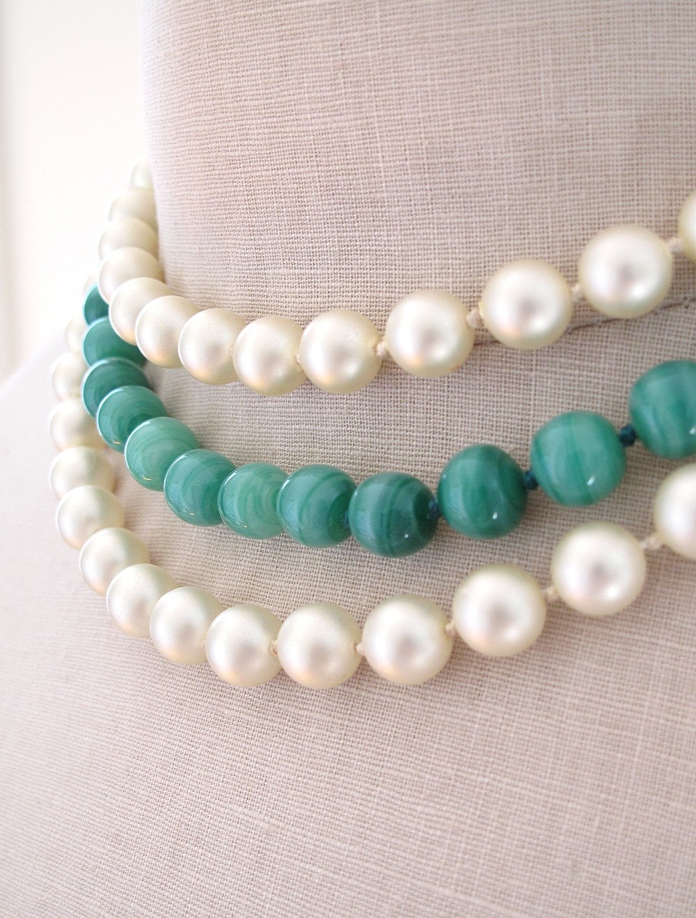 This beautiful three strand necklace sits close to the neck. It is made of two strands of pearls and one strand of green glass beads that resemble Jade. The most beautiful feature of this necklace is the ornate gold clasp with a green bead set in the center. The clasp is 1.25